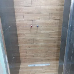 Świeżo wykafelkowana kabina prysznicowa z drewnopodobnymi płytkami na ścianach i podłodze, widoczne krzyżyki dystansowe oraz odpływ liniowy.