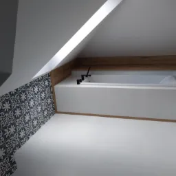 Nowoczesna łazienka na poddaszu z białą wanną obudowaną płytkami, czarną armaturą, dekoracyjnymi płytkami na ścianie i drewnianym blatem.