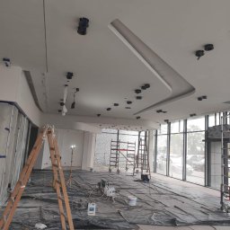 M-4 concept - Malowanie sufitu w biurze, widoczne przygotowania: folia ochronna na podłodze, drabiny, sprzęt malarski i otwory na oświetlenie punktowe w suficie.
