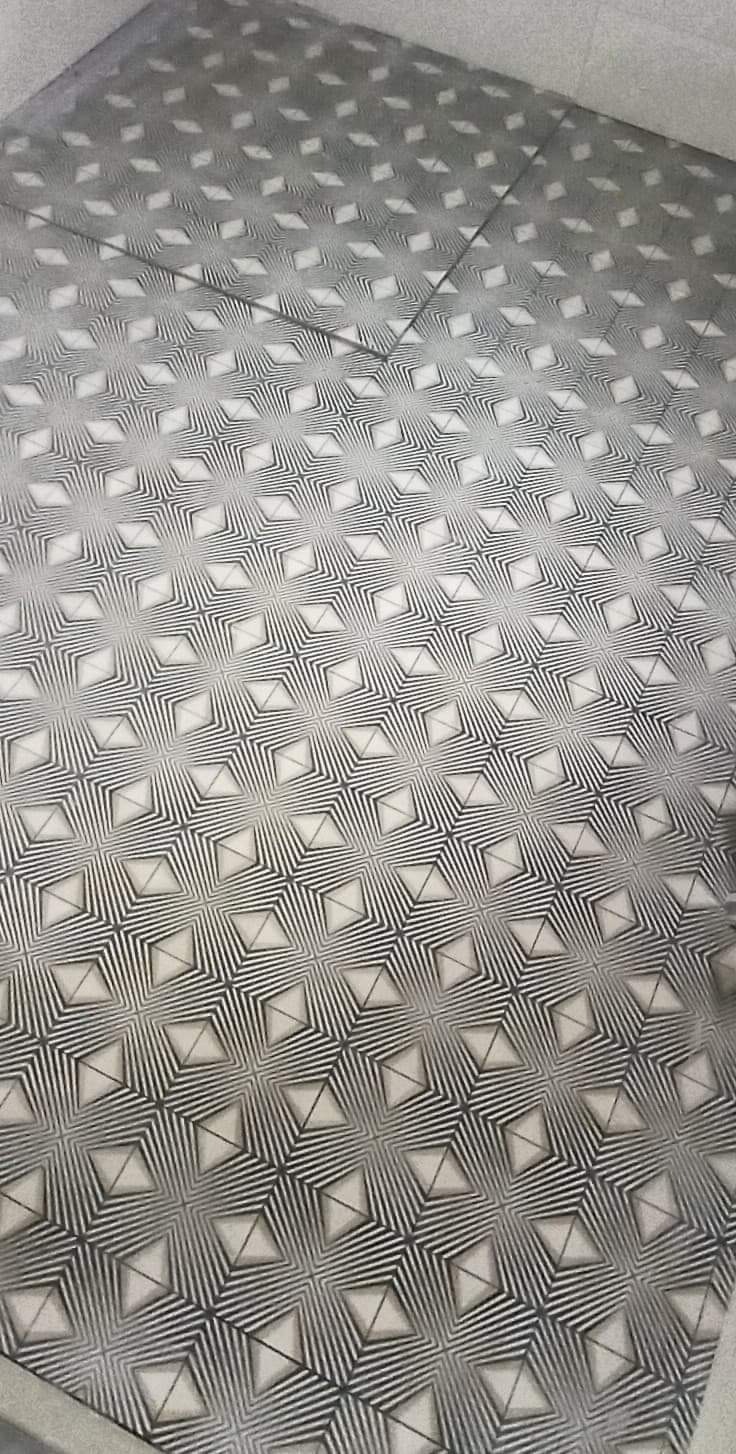 Wzorzysta podłoga wyłożona szarymi i białymi płytkami ceramicznymi ułożonymi w geometryczny wzór gwiazd, widoczne fugi między płytkami.