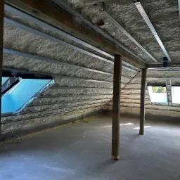 Poddasze po natrysku pianki izolacyjnej, widoczne metalowe profile pod konstrukcję, drewniane słupy i okna dachowe