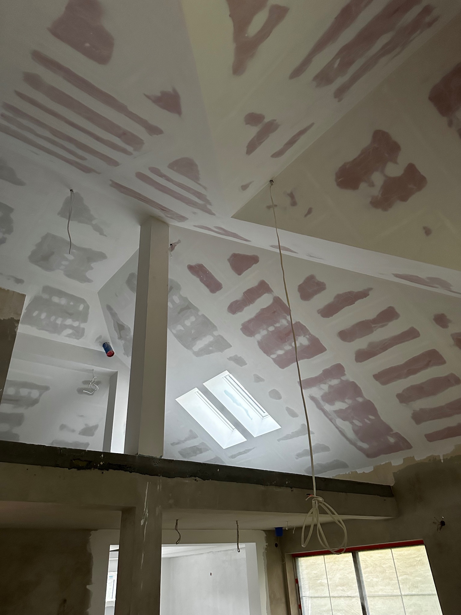 Poddasze w trakcie szpachlowania, widoczne łączenia płyt karton-gips pokryte szpachlą, okno dachowe i przewody elektryczne.