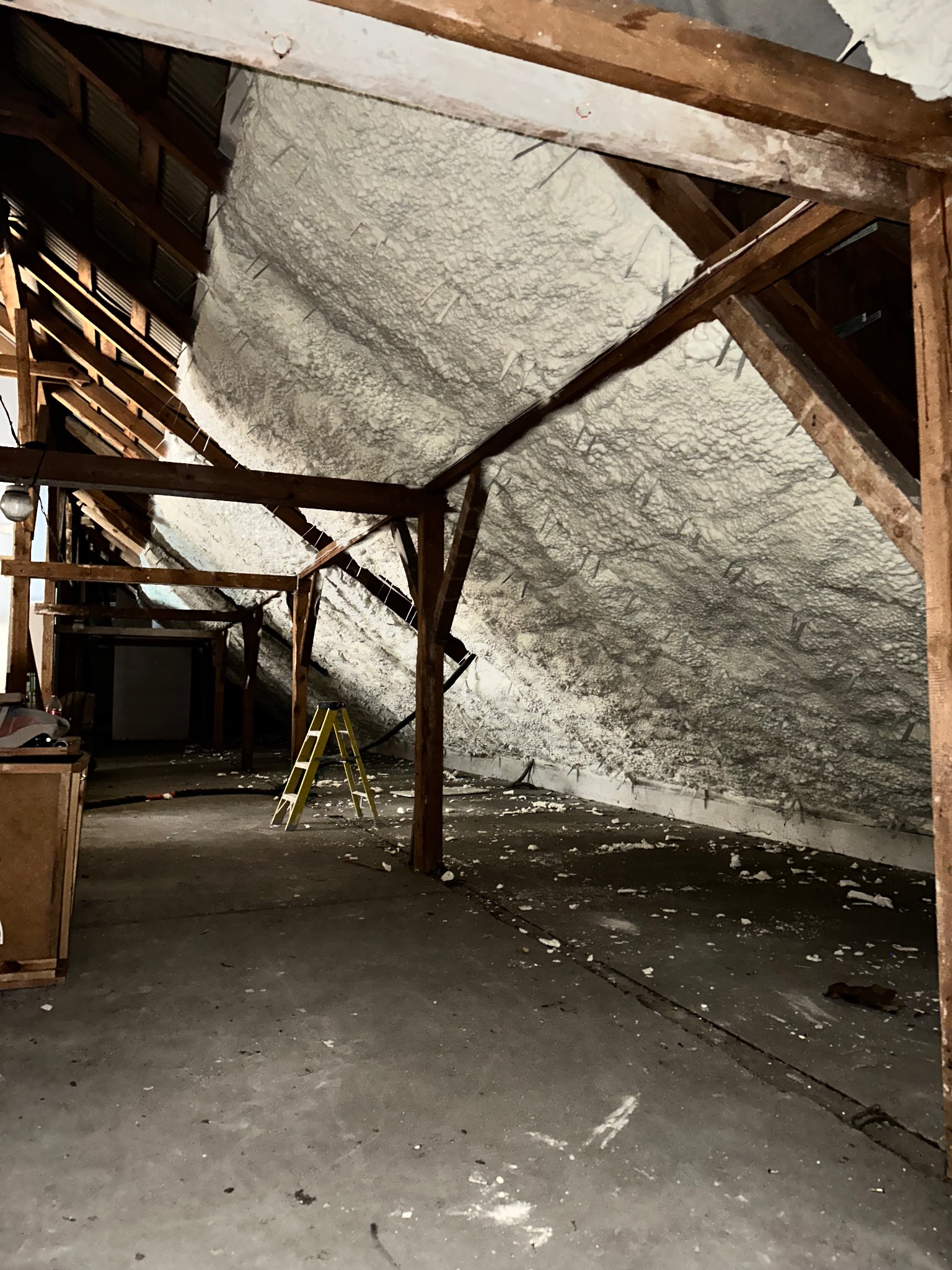 Poddasze po ociepleniu pianką PUR, widoczne drewniane elementy konstrukcyjne i żółta drabina. Pianka pokrywa skośne powierzchnie dachu, tworząc jednolitą warstwę izolacyjną.