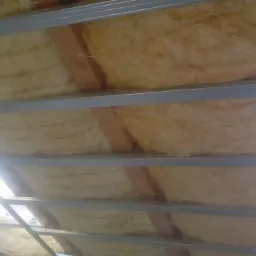 Izolacja z wełny mineralnej zamontowana między metalowymi profilami sufitu podwieszanego, widoczne drewniane elementy konstrukcyjne