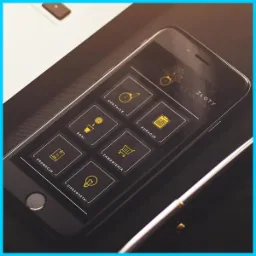 Ekran smartfona prezentujący interfejs aplikacji mobilnej 'Złoty Standard' z ikonami kategorii: Koktajle, Soki, Kuracje, Promocje, Zamówienia i Ciekawostki, umieszczony obok laptopa i pióra.