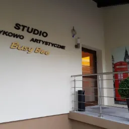 Wejście do studia językowego z napisem 'Studio Językowo Artystyczne Busy Bee', widoczny plakat z motywem Londynu i budką telefoniczną.