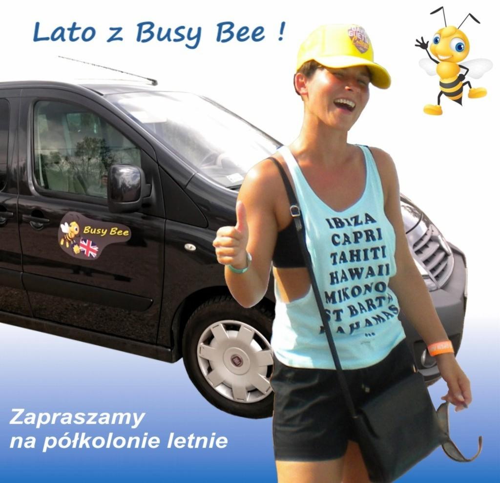 Kobieta w koszulce z nazwami wysp wakacyjnych, kciuk w górę, stoi przed czarnym vanem z naklejką Busy Bee, zapraszamy na półkolonie letnie.
