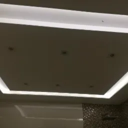 Nowoczesny sufit podwieszany z oświetleniem LED w kształcie kwadratu, z widocznymi punktowymi lampami halogenowymi i fragmentem ściany wykończonej mozaiką.