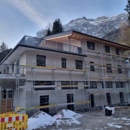 Profi Haus APP Andrzej Paździor - Nowoczesny, dwupiętrowy dom w trakcie budowy, z widocznymi rusztowaniami i częściowo wykończoną elewacją na tle górskiego krajobrazu.