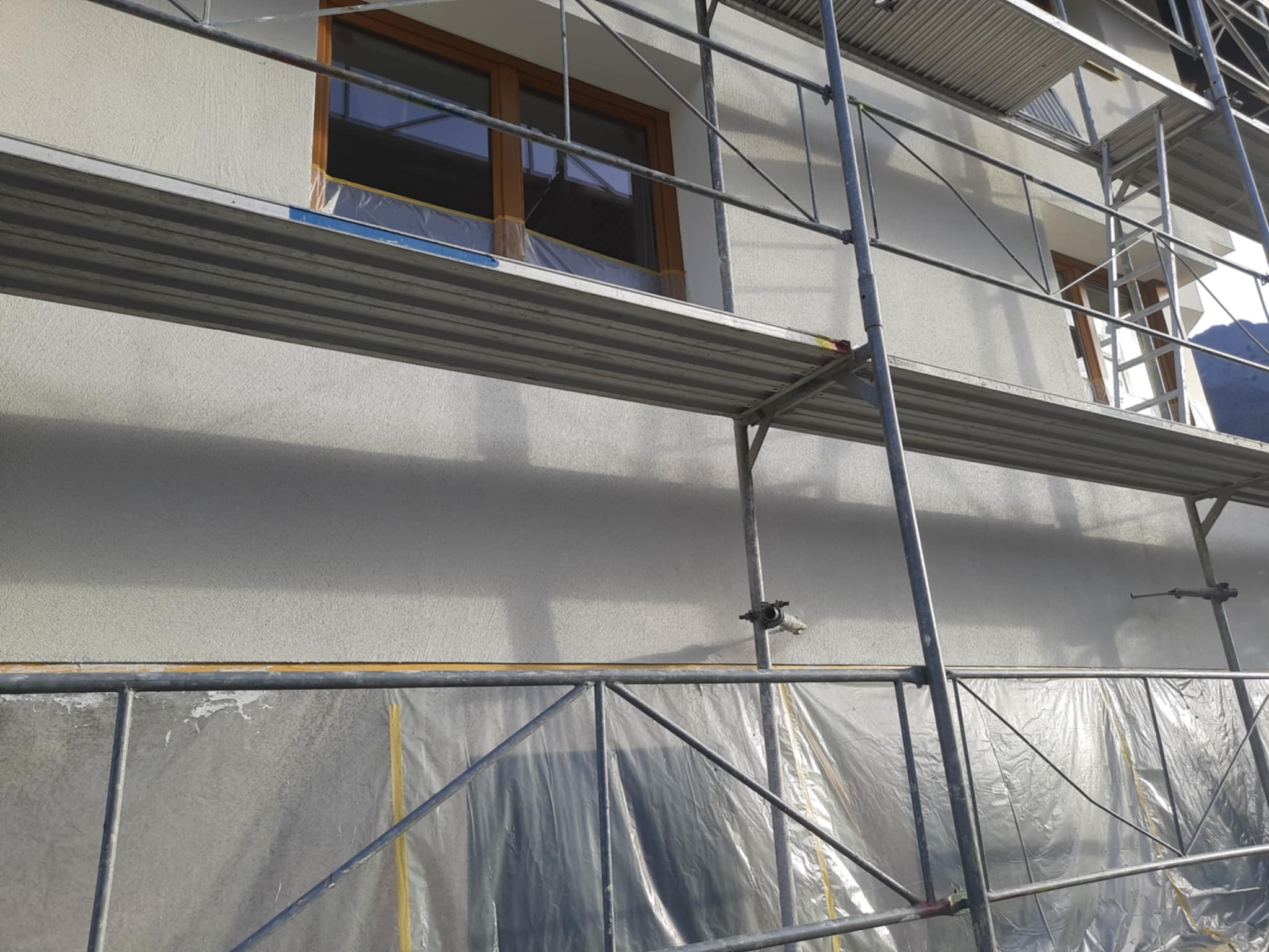 Elewacja budynku w trakcie prac, zabezpieczone okna folią, widoczne rusztowania.