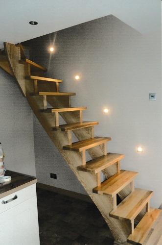 Drewniane schody z oświetleniem punktowym na ścianie, widoczne z boku, z elementami wystającymi zza ściany, w tle fragment blatu kuchennego i szafki.