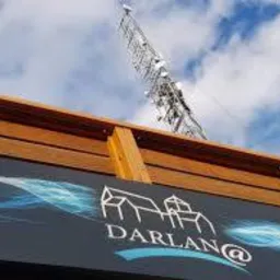 Metalowa wieża telekomunikacyjna widoczna z dołu, zza krawędzi budynku z logo firmy Darlan@