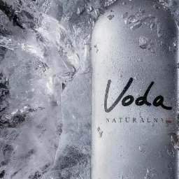 Butelka wody mineralnej z napisem 'Voda Naturalna' otoczona lodem, krople wody na powierzchni butelki, chłodny, orzeźwiający wygląd.