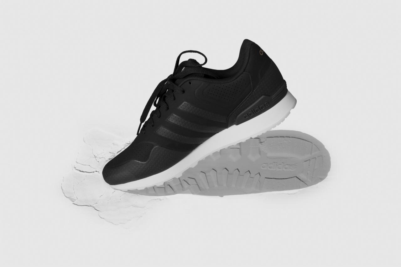 Czarno-białe zdjęcie czarnego buta sportowego marki Adidas na białym tle z odciskiem podeszwy