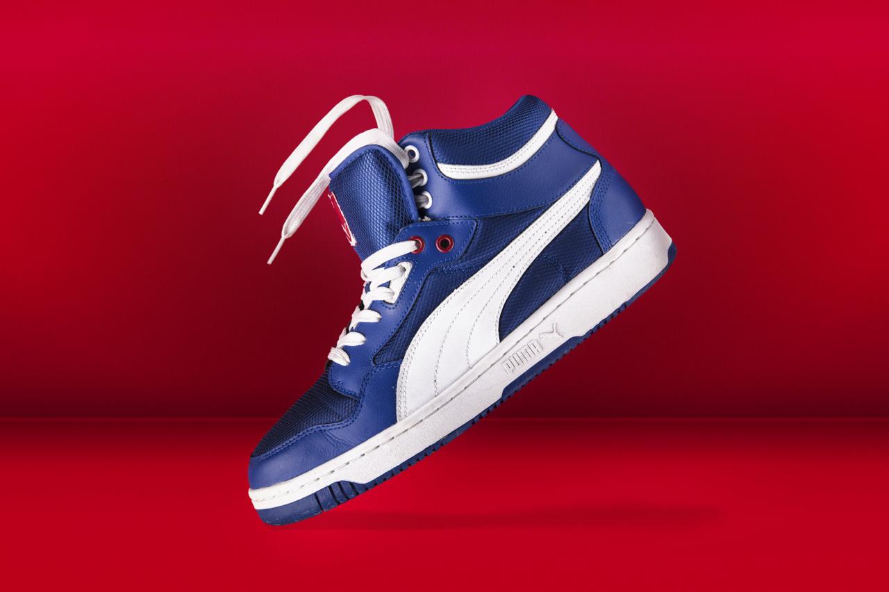 Latający, niebiesko-biały but sportowy Puma na czerwonym tle, z widocznym logo i sznurowadłami