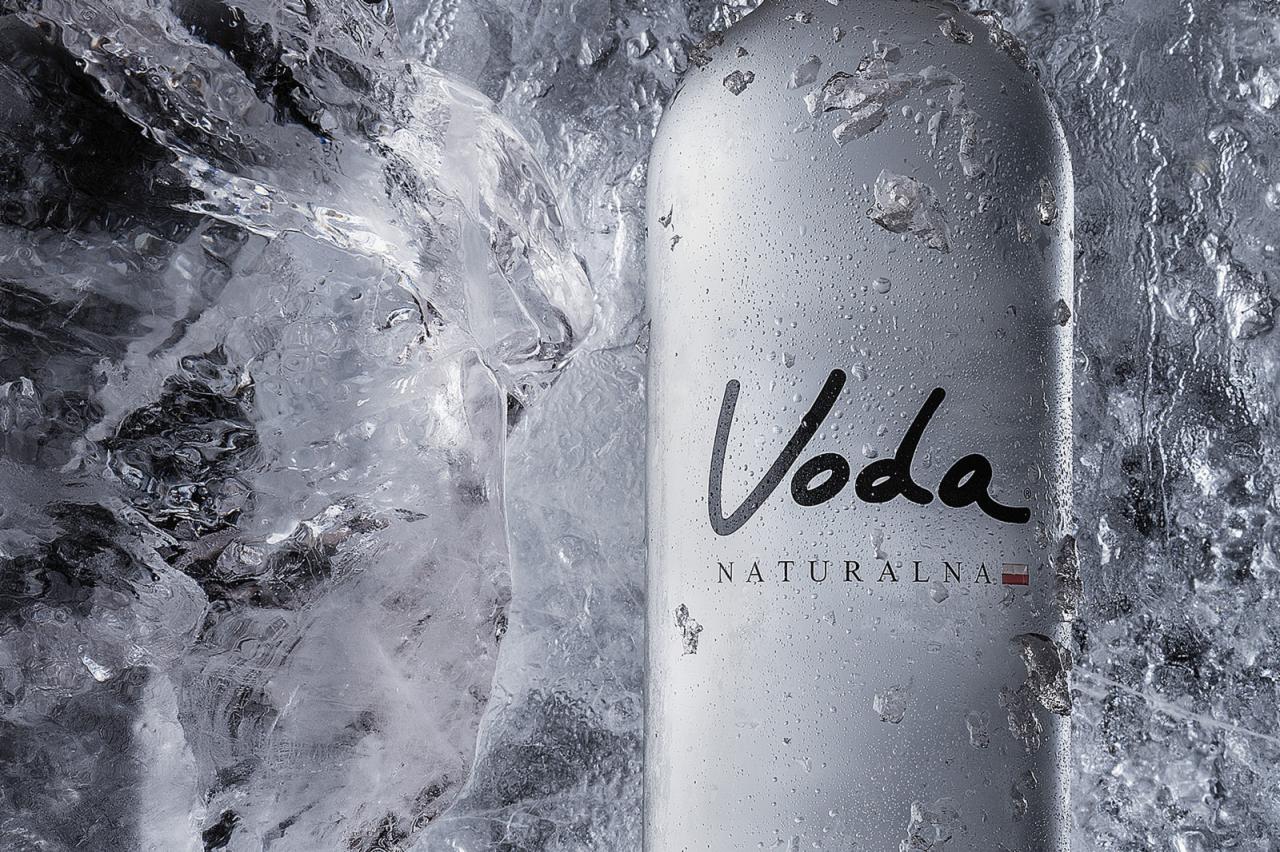 Butelka wody mineralnej z napisem 'Voda Naturalna' otoczona lodem, krople wody na powierzchni butelki, chłodny, orzeźwiający wygląd.