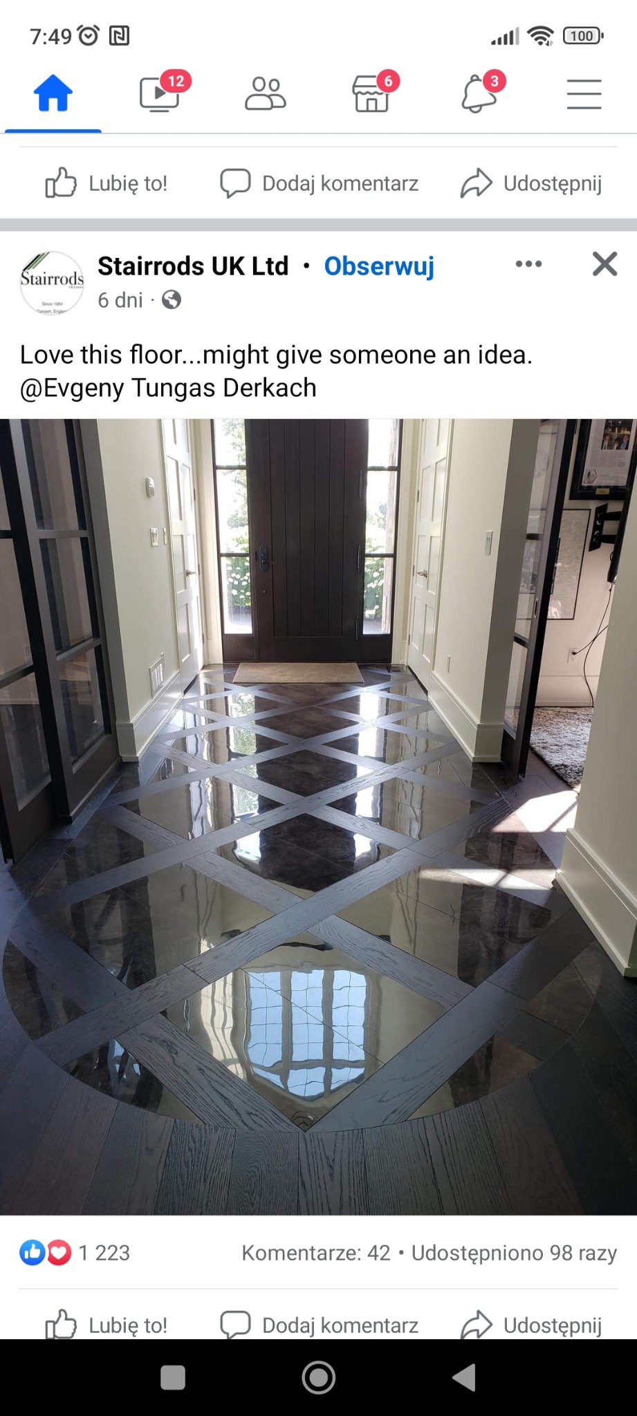 Wypolerowana, ciemna podłoga z drewnianych paneli ułożonych w geometryczny wzór rombów i kwadratów, odbijająca światło okien i drzwi wejściowych.