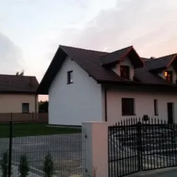 Nowoczesny dom murowany z brązowym dachem i ozdobną bramą w Mysłowicach, sfotografowany o zmierzchu.