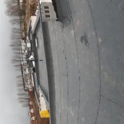 Płaski dach pokryty papą termozgrzewalną z widocznymi kominkami wentylacyjnymi i elementami konstrukcyjnymi, w tle budynek w stanie surowym i zabudowa jednorodzinna