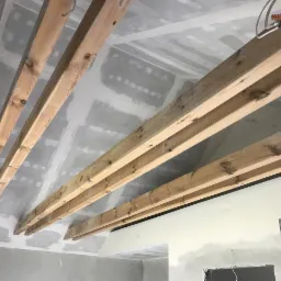 Sufit poddasza w trakcie izolacji: widoczne drewniane belki konstrukcyjne i płyty gipsowo-kartonowe z widocznymi łączeniami przed szpachlowaniem.