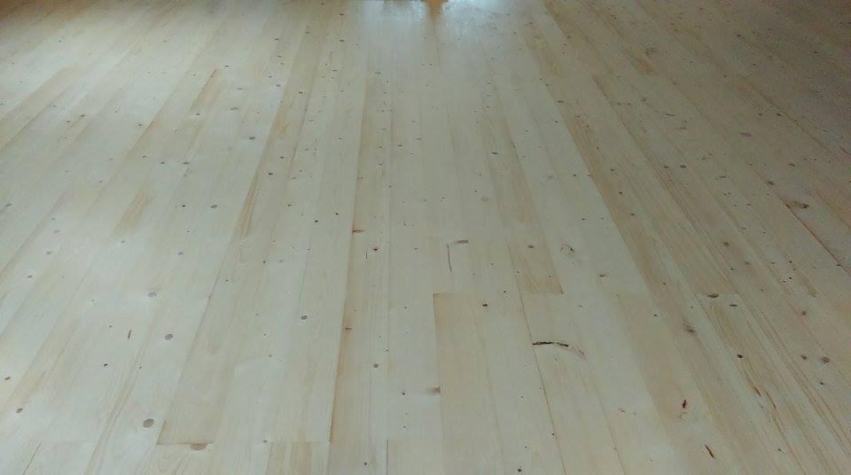 Jasne, świeżo ułożone deski parkietowe z widocznymi naturalnymi słojami i niewielkimi sękami, ułożone równolegle do siebie, oświetlone naturalnym światłem.