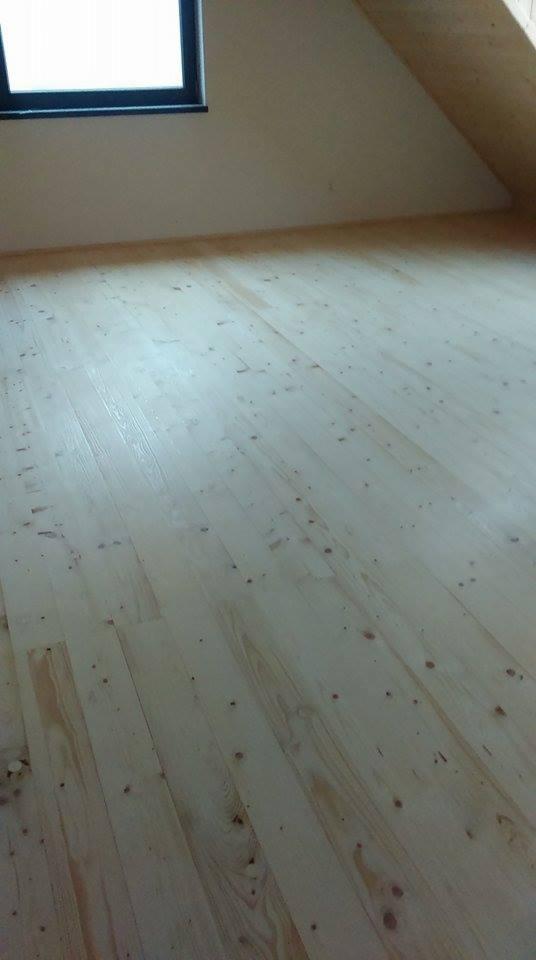 Jasna, drewniana podłoga z widocznymi słojami i sękami w pokoju na poddaszu z oknem.