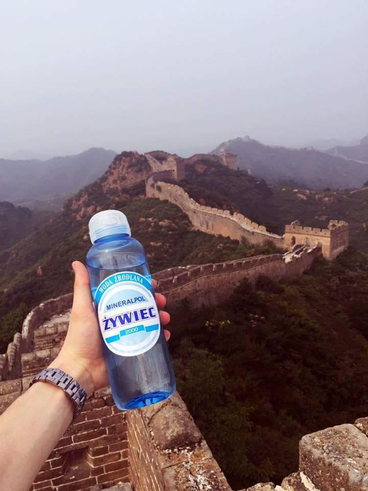 Butelka wody mineralnej Żywiec trzymana na tle fragmentu Muru Chińskiego, widocznego z góry w mglisty dzień.