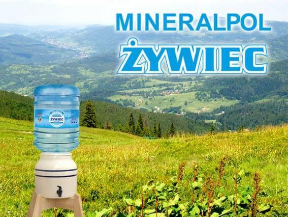 Dystrybutor wody marki Żywiec z pełnym baniakiem na tle górskiego krajobrazu.