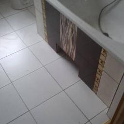 BUD-SOB uslugi ogolno-budowlane - Wykończona obudowa wanny z brązowymi i beżowymi płytkami mozaikowymi, białe płytki podłogowe z szarymi fugami w łazience.