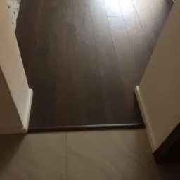 Ułożone panele podłogowe w odcieniach brązu, widoczne przejście między panelami a płytkami podłogowymi z listwą progową.