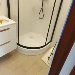 Nowoczesna kabina prysznicowa z czarną armaturą i białą ceramiką w łazience w Stargardzie, widok na umywalkę z szafką i drewnopodobną podłogę.