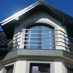 Elewacja domu z balkonem zabezpieczonym prostą, metalową konstrukcją, widok z dołu na tle błękitnego nieba.