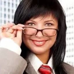 Uśmiechnięta kobieta w okularach, białej koszuli, czerwonym krawacie i szarej marynarce na tle biurowca.