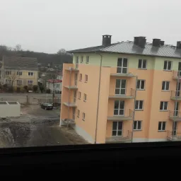 Wielorodzinny budynek w trakcie budowy, z widoczną surową konstrukcją obok pomalowanej, częściowo wykończonej elewacji z balkonami.