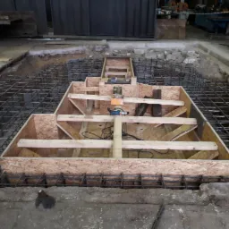 Przygotowanie zbrojenia i szalunku pod nietypowy fundament w Suszcu, widoczny wykop i narzędzia.