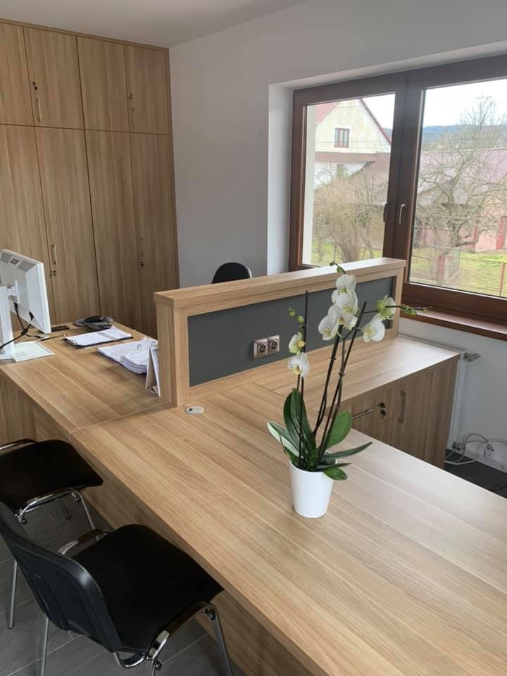 Jasne biuro z drewnianymi meblami, komputerem, dokumentami i storczykiem w doniczce na biurku, widok z okna na wiejski krajobraz.