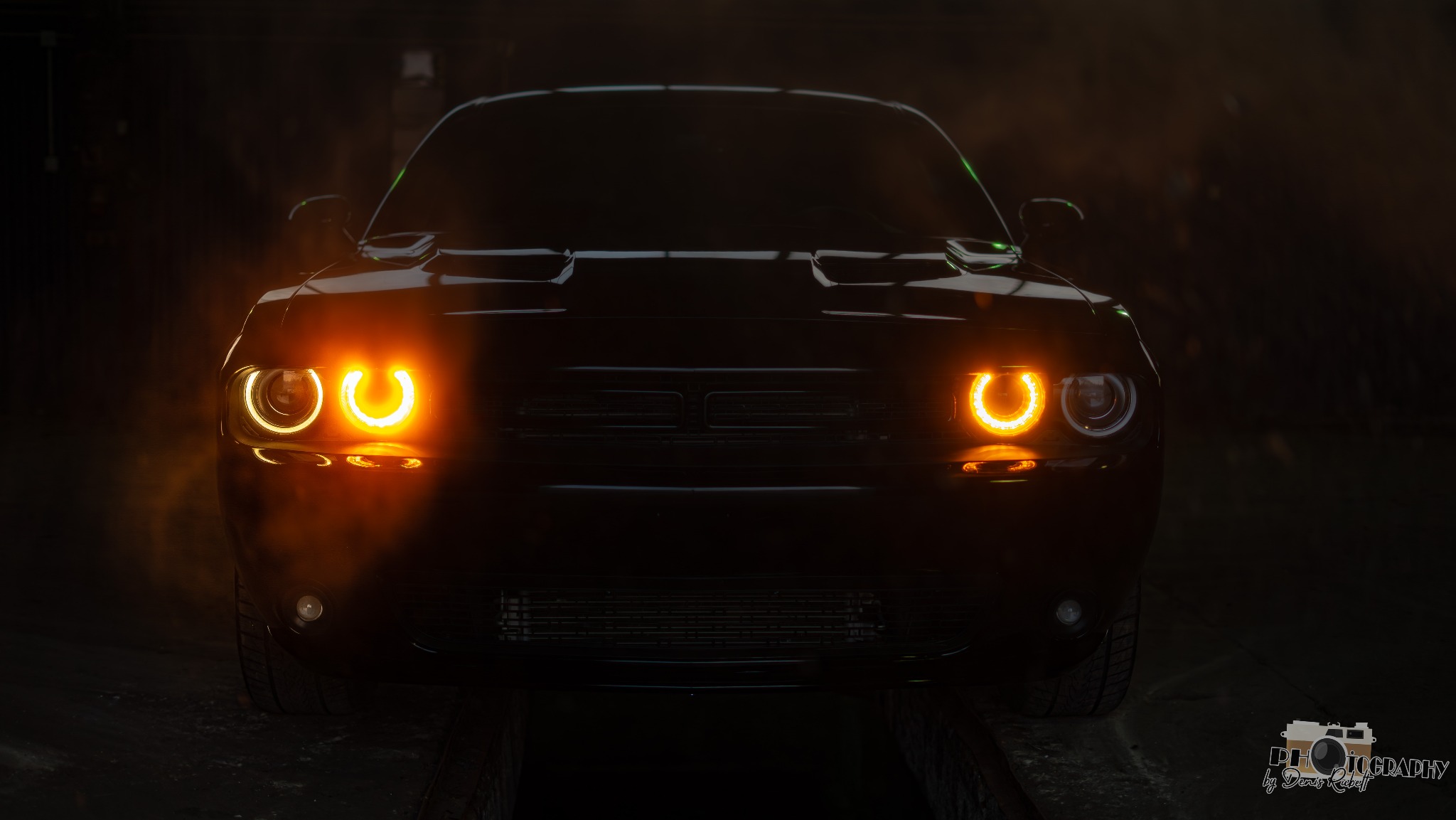 Ciemny, sportowy samochód z włączonymi, okrągłymi światłami przednimi, sfotografowany z niskiego kąta w słabym oświetleniu.