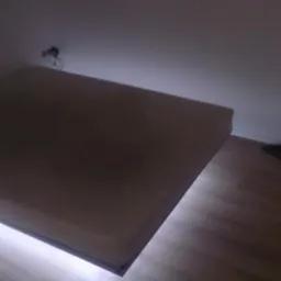 Płyta kartonowo-gipsowa zamontowana na ścianie, podświetlona od spodu, widoczne ślady po wierceniu w ścianie i fragment podłogi z panelami.