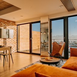 Firma Patryk Gacek - Jasne wnętrze apartamentu z ceglaną ścianą, drewnianym stołem jadalnym i widokiem na góry przez panoramiczne okna.