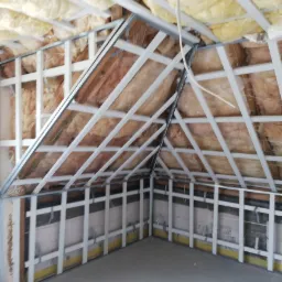 Poddasze w trakcie adaptacji: widoczne ocieplenie wełną mineralną między krokwiami oraz konstrukcja metalowa pod płyty gipsowo-kartonowe na ścianach i suficie.