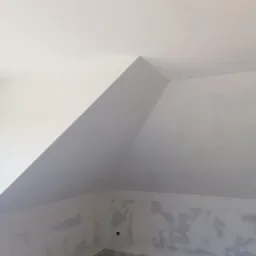 Poddasze w trakcie przygotowania do malowania, widoczne ślady po szpachlowaniu na skośnych ścianach i suficie, gniazdko elektryczne w ścianie