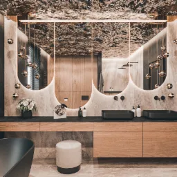 Luksusowa łazienka z czarną wanną, umywalkami nablatowymi i lustrami z podświetleniem LED, dekoracyjnym sufitem i złotymi lampami kulami.