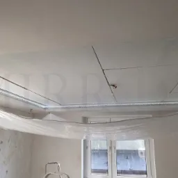 Montaż podwieszanego sufitu z płyty karton gips z oświetleniem LED, zabezpieczonego folią malarską podczas prac wykończeniowych ścian, widoczna drabina malarska.