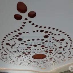Biały sufit napinany z unikalnym, brązowym wzorem z okrągłych otworów, tworzącym dekoracyjny motyw. Oświetlenie LED wzdłuż krawędzi podkreśla design.