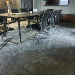 Szara, teksturowana podłoga w biurze pod nowoczesnym stołem konferencyjnym z czarnymi krzesłami na chromowanych nogach.