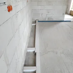 Wewnętrzna instalacja elektryczna w surowym budynku, widoczne kable w peszlach i puszki w ścianie z betonu komórkowego, przygotowane do dalszych prac wykończeniowych.