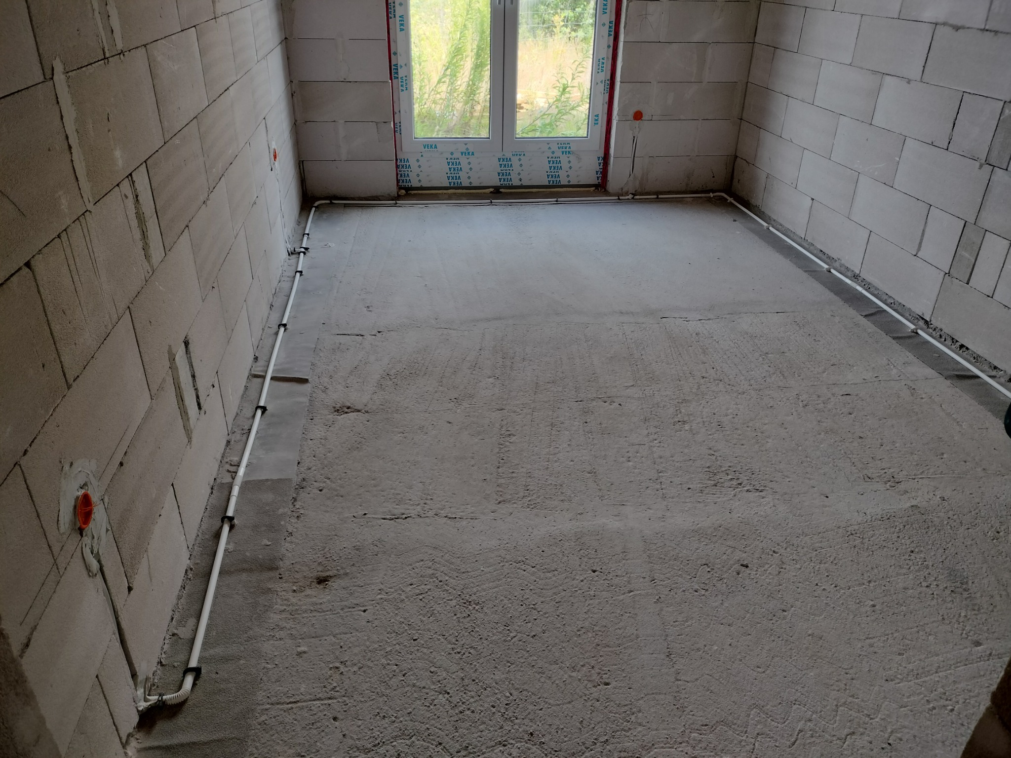 Surowy pokój z instalacją elektryczną w listwach przypodłogowych i puszkami w ścianach z betonu komórkowego. Widoczne okno z PCV.