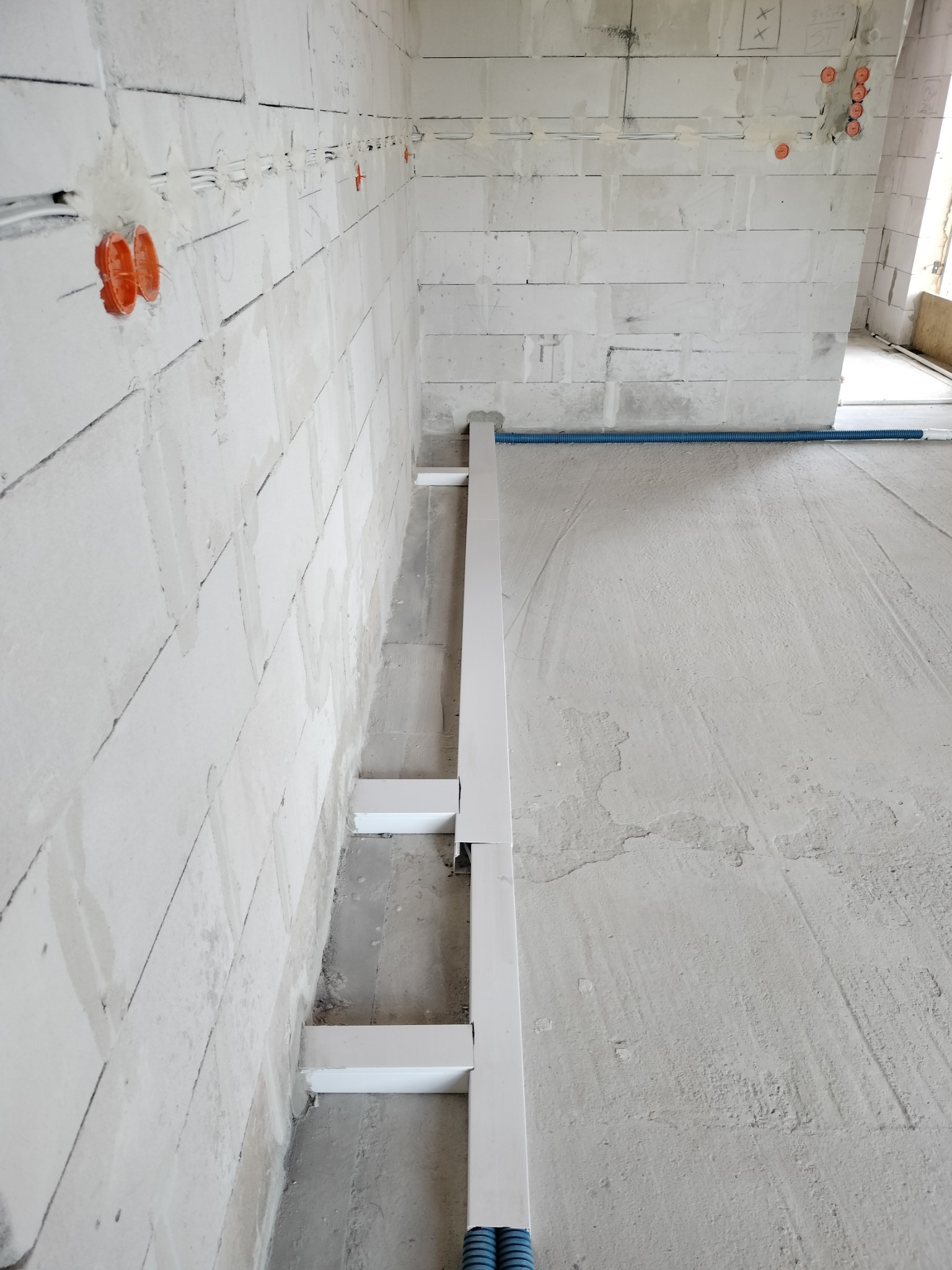 Wewnętrzna instalacja elektryczna w surowym budynku, widoczne kable w peszlach i puszki w ścianie z betonu komórkowego, przygotowane do dalszych prac wykończeniowych.