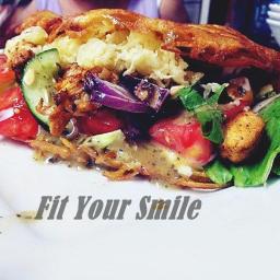 Dominika Malinowska - Otwarta kanapka z warzywami, w tym pomidorami, ogórkiem, czerwoną cebulą i sałatą, polana sosem, z widoczną chrupiącą warstwą wierzchnią i napisem 'Fit Your Smile'.