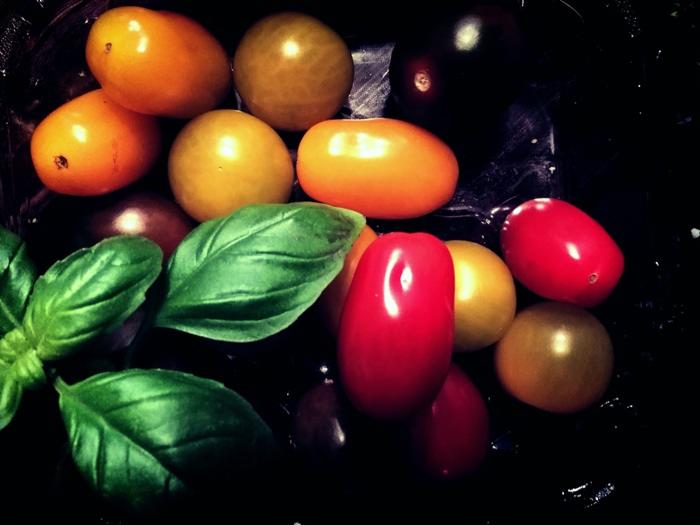 Kompozycja z różnokolorowych pomidorków koktajlowych i świeżej bazylii na ciemnym tle, z wyraźnymi refleksami światła.